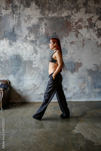 Obraz na płótnie A beautiful red-haired girl in sexy lingerie and black pants poses in a concrete room. w salonie