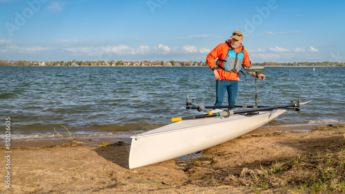 Senior male rower with his rowing shell on a beach of Boyd Lake in northern Colorado, serly spring scenery photo