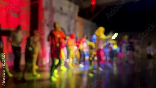 Blurred crowd of kids dancing on the dance floor of theatre stage under the light of colored spotlights and laser. Young kids jump and raise their hands up