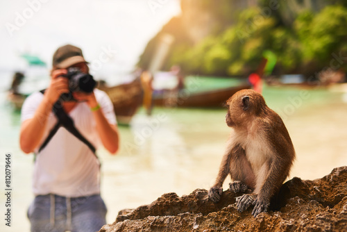 Man, camera and monkey with sunshine, beach and tropical island with getaway trip, Bali and seaside. Person, photographer and tourist with memory, travel and summer with wild animal and adventure photo