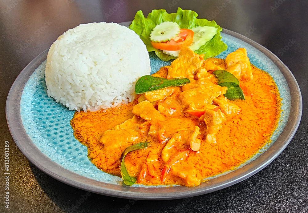A vibrant plate of red curry with chicken, served alongside a mound of white rice and fresh salad A vibrant plate of red curry with chicken, served alongside a mound of white rice and fresh salad