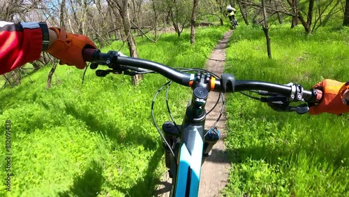 Two cyclists riding on a forest trail on mountain bikes. First-person view.