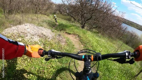 Two cyclists riding on a forest trail on mountain bikes. First-person view.