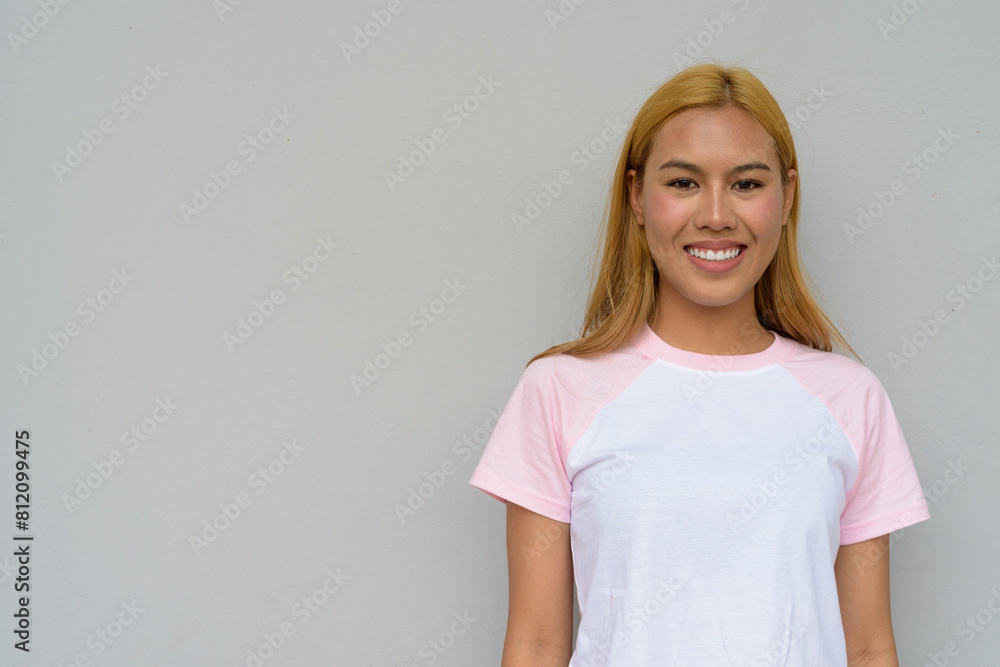 Obraz premium Portrait of beautiful Asian girl with blonde hair smiling against plain background