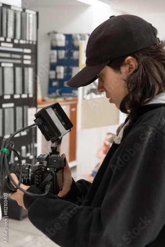 Imagen vertical de trabajadora joven con gorro filmando con cámara en jaula y monitor