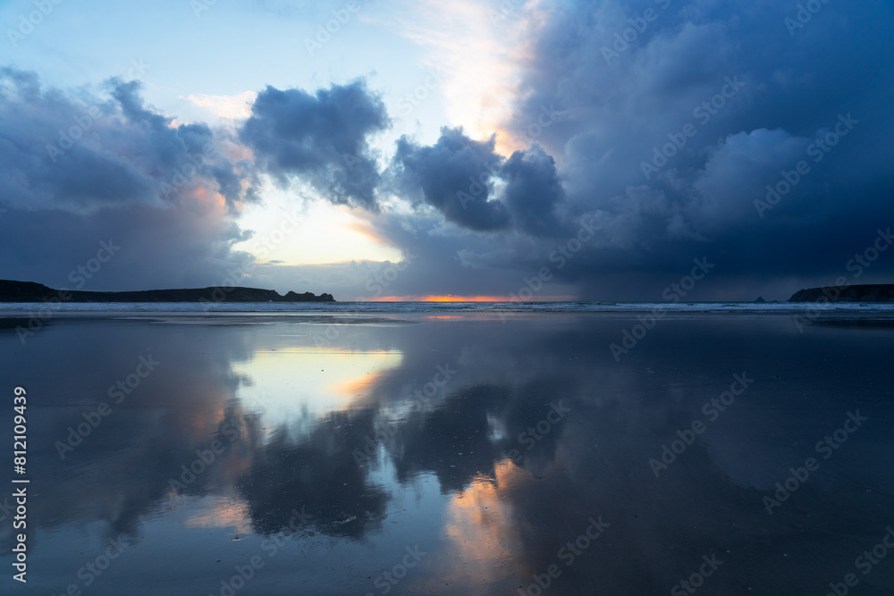 Les nuages menaçants reflètent leurs teintes sur le sable mouillé d'une plage de la presqu'île de Crozon en Bretagne, dans un décor envoûtant au coucher du soleil.