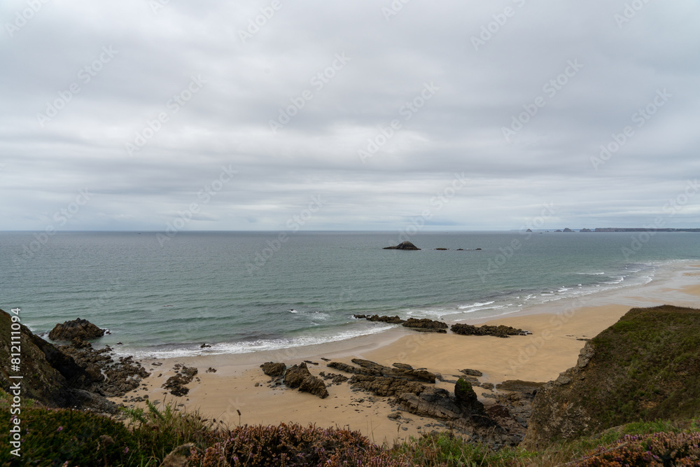 Falaises escarpées, plage de sable et sillon rocheux, sous un ciel couvert, offrant une vue saisissante sur la mer d'Iroise et l'île de Guénéron depuis la presqu'île de Crozon Falaises escarpées, plage de sable et sillon rocheux, sous un ciel couvert, offrant une vue saisissante sur la mer d'Iroise et l'île de Guénéron depuis la presqu'île de Crozon
