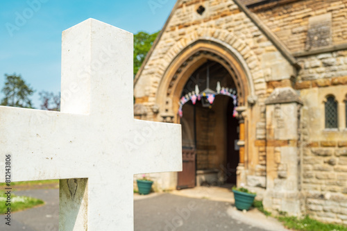 Shallow focus of a marble crucifix seen outside a typical English church. Union Jack bunting can be seen within the entrance  the church celebrating its centenary.