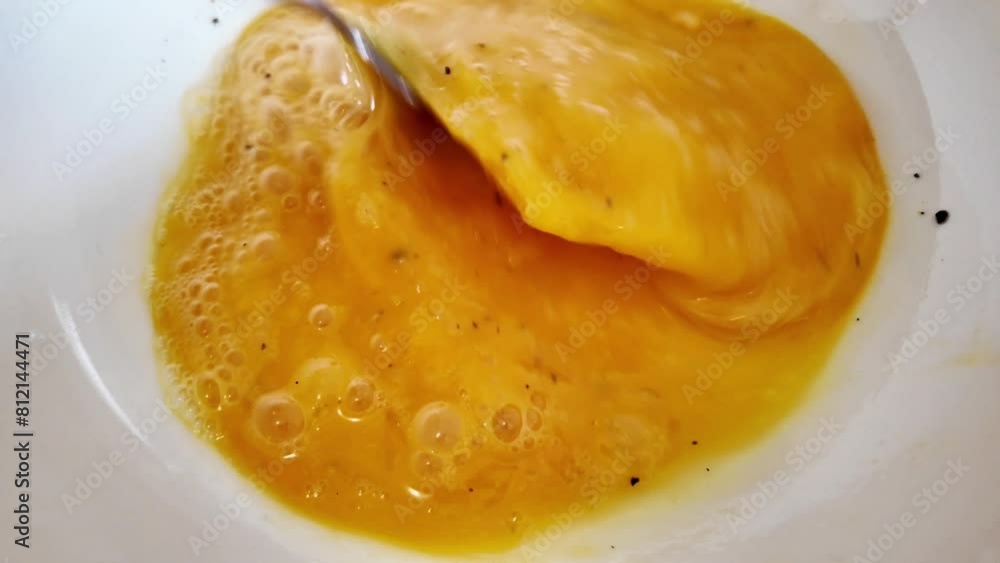 Whisked fresh eggs with pepper in a white bowl, concept related to cooking, baking, and Easter holiday food preparation related to culinary arts and home cooking