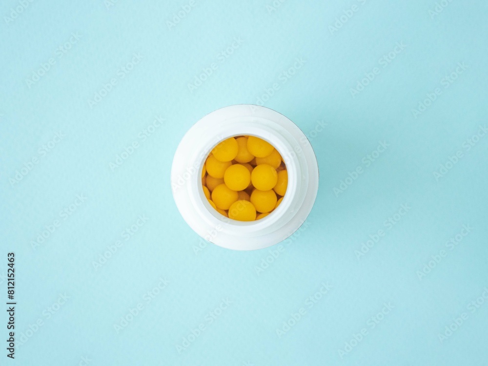 Top view of a plastic white jar with yellow round vitamin tablets on a blue background, a place for text Top view of a plastic white jar with yellow round vitamin tablets on a blue background, a place for text