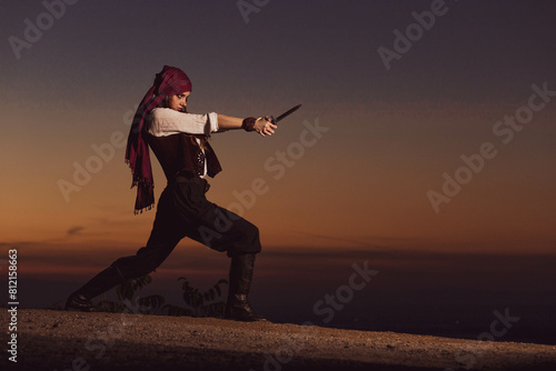 Outdoor portrait of young female in pirate costume holding a knife. Copy space
