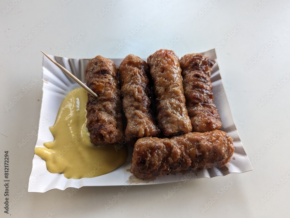 Mici cu mustar and a toothpick on a paper plate. Traditional romanian fast food.