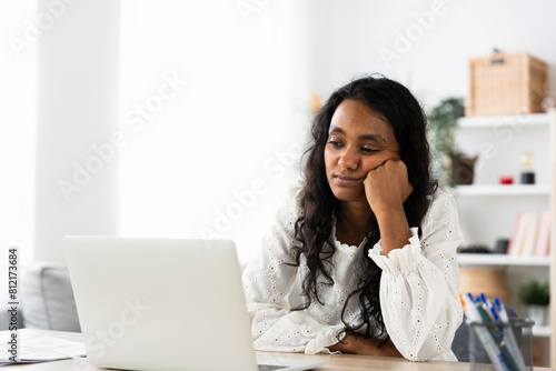 Bored Indian student watching tutorial on laptop. Young woman having online class at home.