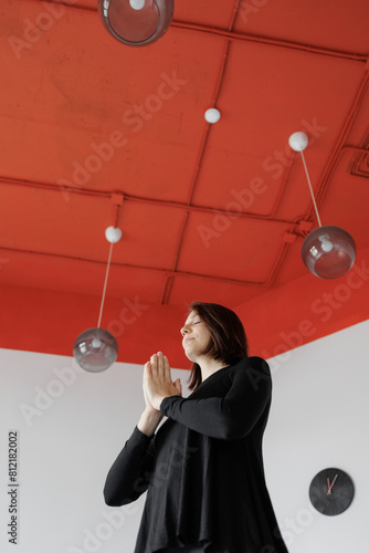 woman meditates and practices yoga, hands above her head against background of red ceiling in sports studio. Spiritual, mental health, stretching and flexibility. Breathing practice. Healthy lifestyle