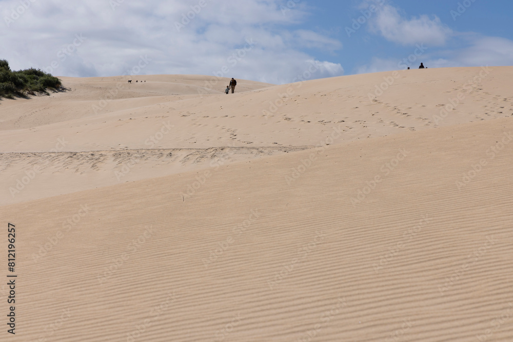 People trekking on foot walking up sand dune on a bright sunny day with blue sky at Punta Paloma People trekking on foot walking up sand dune on a bright sunny day with blue sky at Punta Paloma