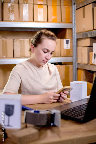 Young entrepreneur small business checking internet orders on smartphone and preparing boxed items for delivery to customers