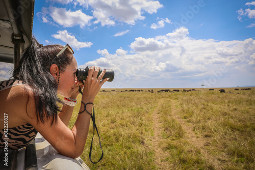 Photography A girl observing a grazing herd of buffaloes through binoculars in the Masai Mara National Park, Kenya