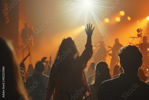 A silhouette of a dynamic crowd at a concert, with a central figure raising their hand towards a brightly lit stage