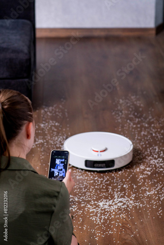Woman using an app on his phone paired with a robotic cleaner. Display with apartment map, cleaning and power status.