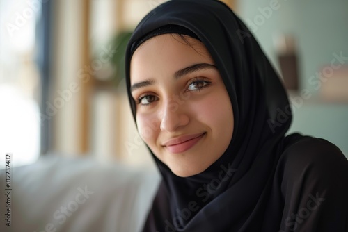 A portrait of a young woman wearing a hijab, capturing her gentle smile and kind eyes in a well-lit room