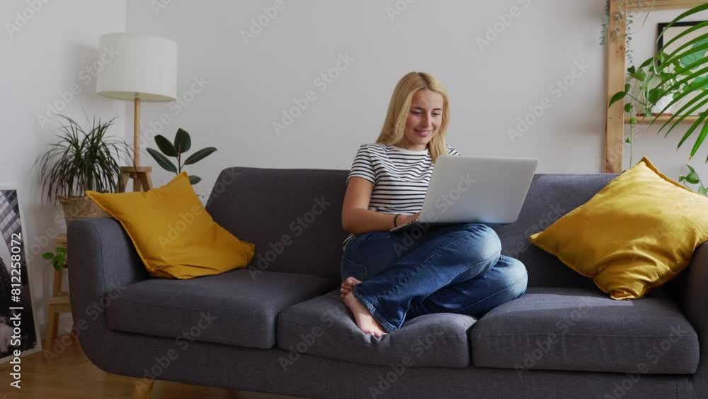 Beautiful young woman working on laptop computer while sitting on sofa in the living room. Millennial pretty student girl studying online. Beautiful young woman working on laptop computer while sitting on sofa in the living room. Millennial pretty student girl studying online.