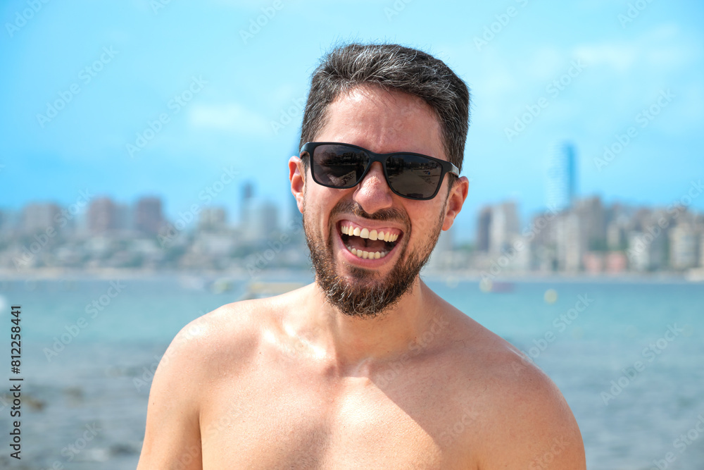 Young Hispanic man model smiling with sunglasses on beach looking to camera Young Hispanic man model smiling with sunglasses on beach looking to camera