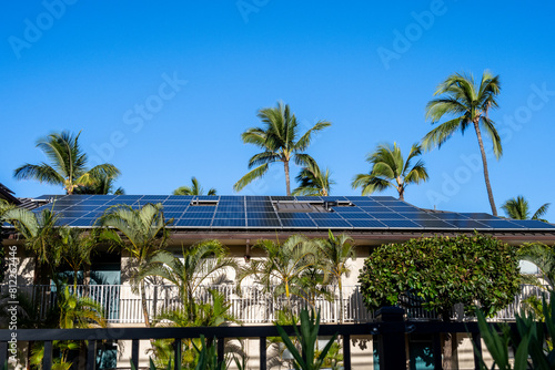 Condo building roof covered in solar panels to generate green alternative energy on sunny Maui, in contrast to the utility power distribution lines in front 