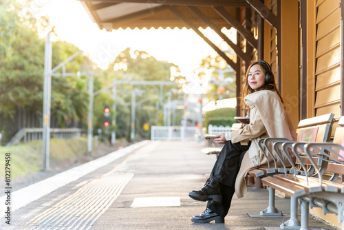 Photography Asian woman listening to music with headphones and mobile phone app during waiting for train in the city