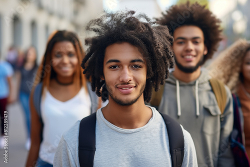Portrait of a confident young man with curly hair smiling at the camera, accompanied by a group of diverse friends casually strolling down an urban street, depicting friendship and diversity photo