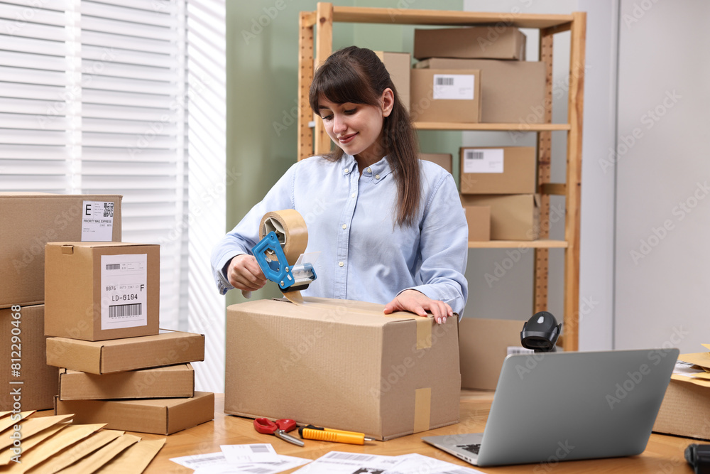 Parcel packing. Post office worker taping box at wooden table indoors Parcel packing. Post office worker taping box at wooden table indoors