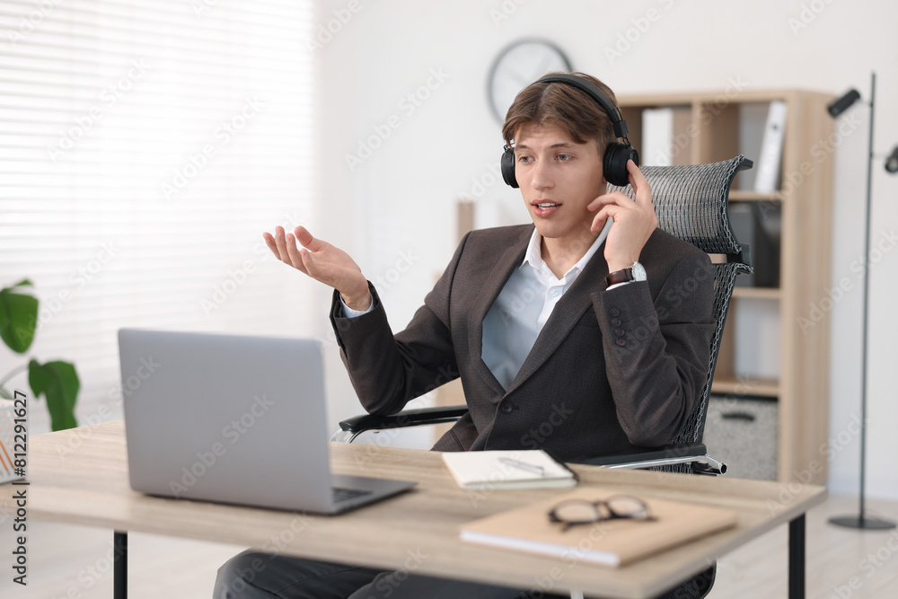 Man in headphones using video chat during webinar at wooden table in office Man in headphones using video chat during webinar at wooden table in office