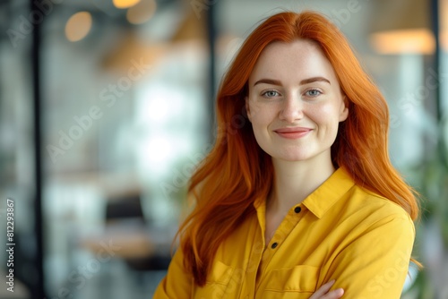 Wallpaper Mural Professional portrait of a smiling young woman with striking red hair, dressed in a stylish yellow blouse, posing confidently in a modern office environment with a blurred background Torontodigital.ca