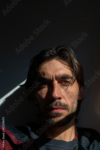 hombre serio con mirada al frente, con su rostro iluminado desde su lateral izquierdo en un fondo negro oscuro  photo