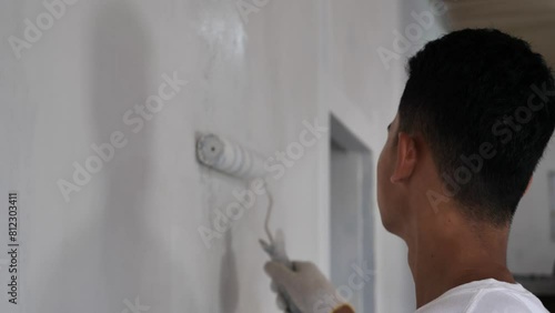 Asian male painter painting new white wall with roller brush, house interior renovation