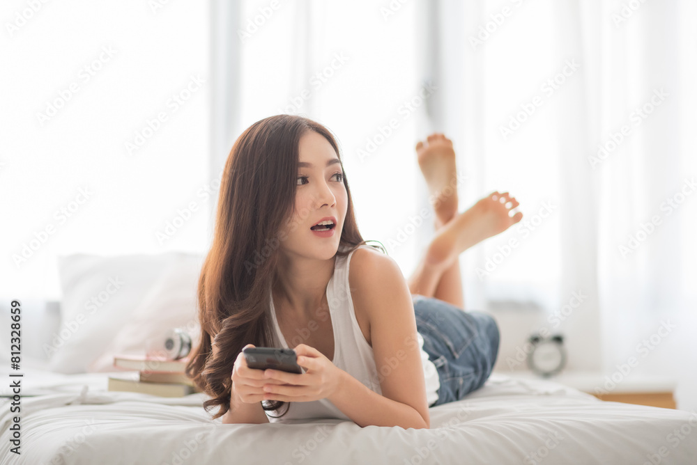 Candid Portrait of Beautiful Asian Korean woman using smartphone while lying on her bed at home. Candid Portrait of Beautiful Asian Korean woman using smartphone while lying on her bed at home.