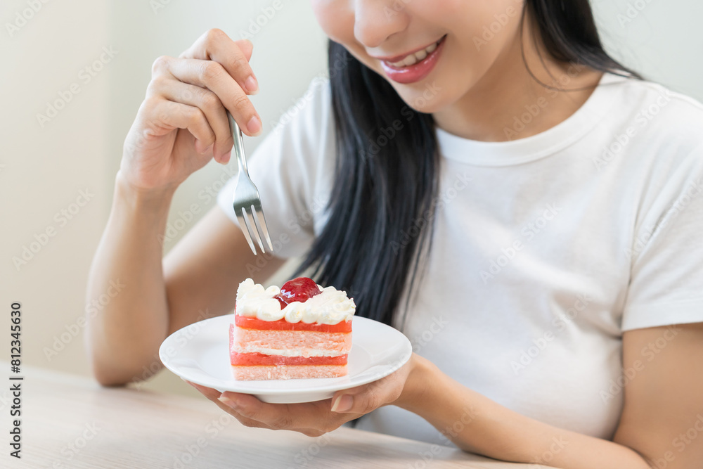 Smiling happy asian young woman holding fork eating slice piece chiffon strawberry layer cake sitting at table, girl eat sweet or dessert cake. Enjoying healthy fast food unhealthy choice concept. Smiling happy asian young woman holding fork eating slice piece chiffon strawberry layer cake sitting at table, girl eat sweet or dessert cake. Enjoying healthy fast food unhealthy choice concept.