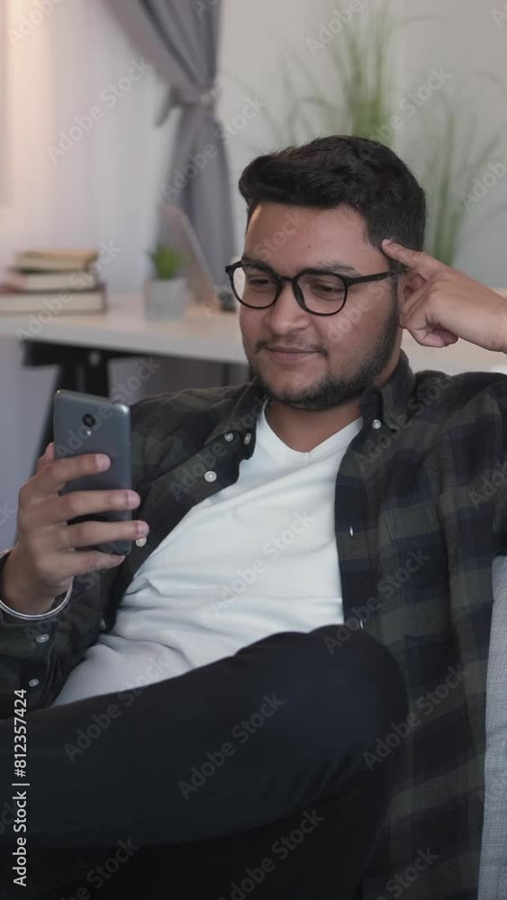 Vertical video. Online call. Virtual communication. Device leisure. Cheerful man talking on cell phone social media internet chat on cozy sofa in home living room. Vertical video. Online call. Virtual communication. Device leisure. Cheerful man talking on cell phone social media internet chat on cozy sofa in home living room.