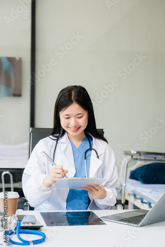 Confident young  female doctor in white medical uniform sit at desk working on computer. Smiling use laptop
