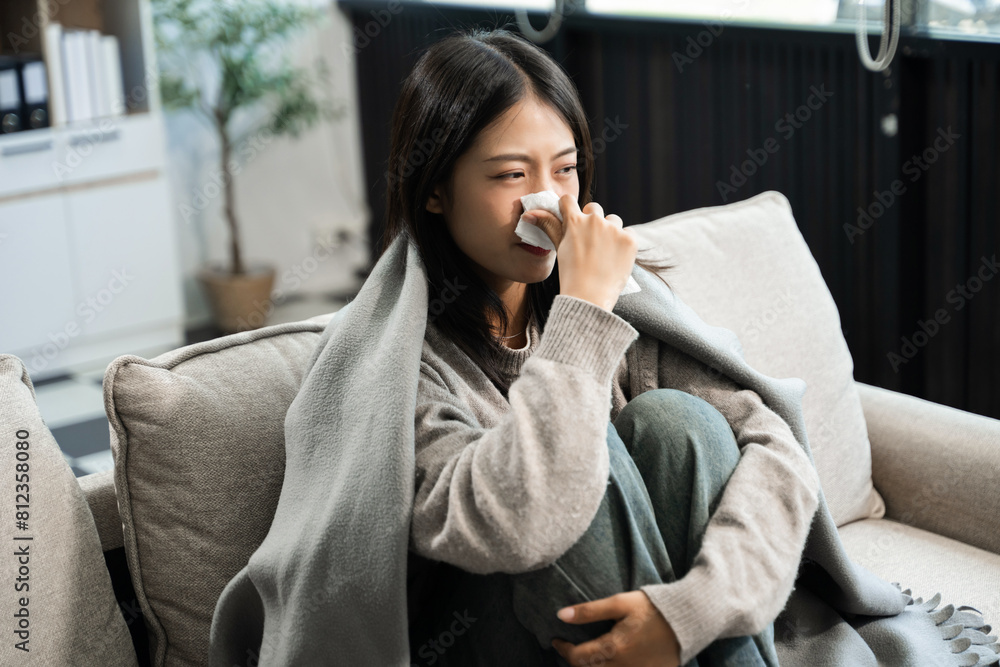 Young Asian woman suffering from flu symptoms, covered with a blanket on a sofa. Concept of illness, healthcare, and recovery Young Asian woman suffering from flu symptoms, covered with a blanket on a sofa. Concept of illness, healthcare, and recovery