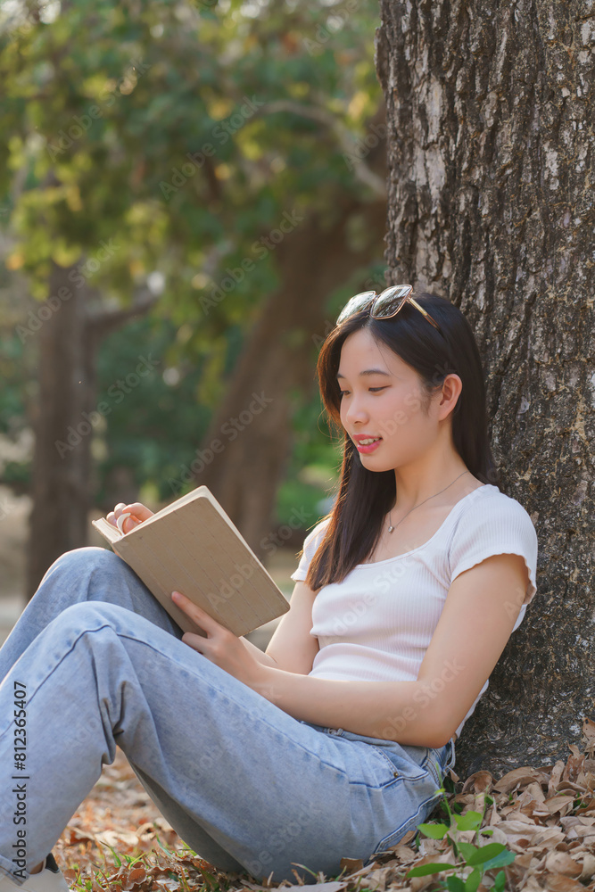 Obraz premium Young asian women sitting on grass to leaning the tree and reading a literature book with recreation happiness while enjoying to relaxation with journey travel trip lifestyle in the nature park