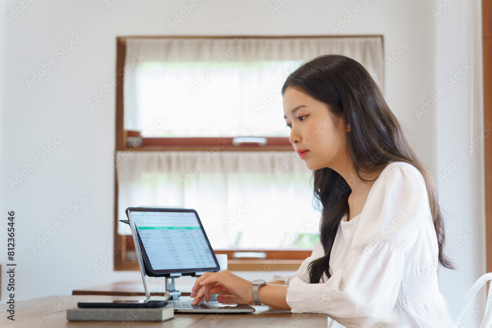 Young asian businesswoman typing business report on laptop and reading financial data on tablet while analysis strategy about investment and planning of new startup project to working in cafe Young asian businesswoman typing business report on laptop and reading financial data on tablet while analysis strategy about investment and planning of new startup project to working in cafe
