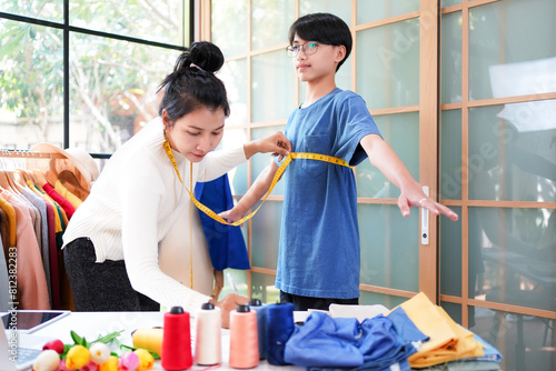 Asian women fashion designer  working and measure the customer in the showroom,  Lifestyle Stylish tailor clothing design and cutting cloths in studio.  Business small Concept