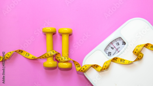 Weight loss control planning.  White scale and measuring tape with dumbbell for body dieting healthy life. Pink background. Top view copy space for banner