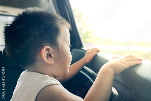 Asian baby boy with light brown clothes looking from car window to ouside with warm sunshine in summer day, view from side