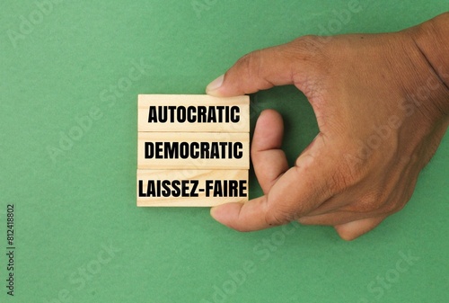 hand holding a stick with the three words of three main management styles, namely Autocratic, Democratic, and Laissez-Faire.