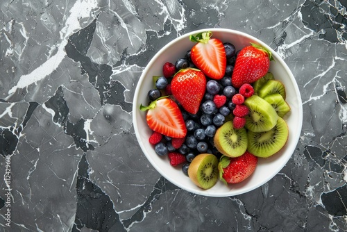 A white bowl filled with strawberries  blueberries  and kiwi slices placed on a marble counter
