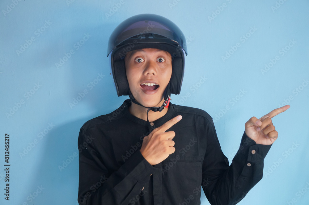 Asian young man wearing motorbike helmet pointing to the side Asian young man wearing motorbike helmet pointing to the side