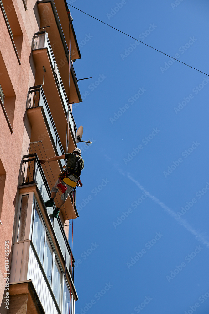 high-rise work on an apartment building. A construction worker inspects the condition of an apartment building for planned reconstruction using climbing equipment high-rise work on an apartment building. A construction worker inspects the condition of an apartment building for planned reconstruction using climbing equipment