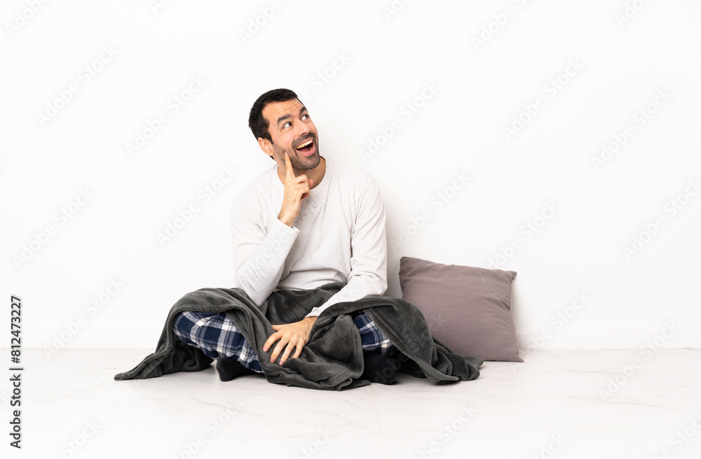 Caucasian man in pajamas sitting on the floor at indoors thinking an idea while looking up Caucasian man in pajamas sitting on the floor at indoors thinking an idea while looking up
