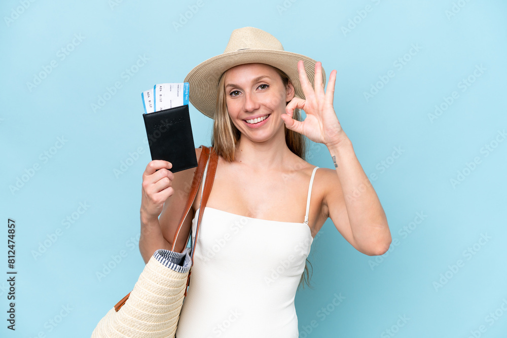 Young blonde woman in swimsuit holding passport isolated on blue background showing ok sign with fingers Young blonde woman in swimsuit holding passport isolated on blue background showing ok sign with fingers